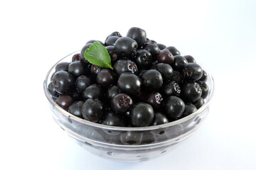Fresh ripe aronia berries decorated with a green leaf in a glass bowl, white background, isometric view