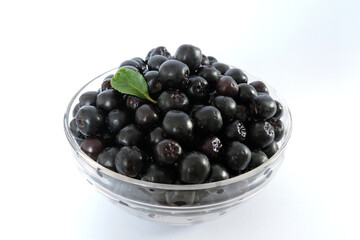 Fresh ripe aronia berries decorated with a green leaf in a glass bowl, white background, isometric view