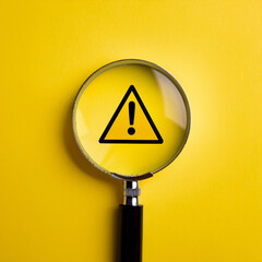 Warning triangle sign and magnifying glass on a yellow background. Close-up.