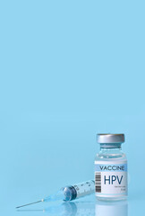 HPV Vaccine in a bottle with a syringe on a blue background. Experimental HPV vaccine vial for...