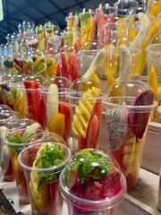Assorted fruit cups with dragon fruit, pineapple, watermelon, and bananas in clear containers. Vibrant colors, market setting, freshness concept