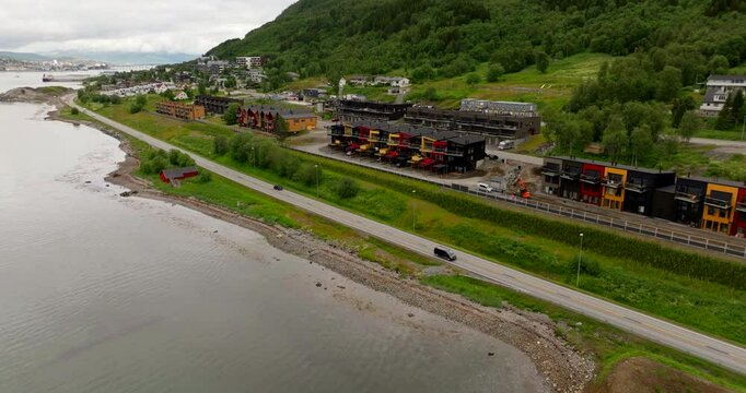 Aerial pullback as cars pass driving along E8 highway by the coastal waters below new modern townhomes