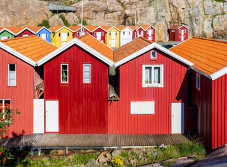 Colorful wooden boathouses lined up against the rocky cliff along the sea channel in the old fishing harbor of Smögen, Sweden, on a sunny summer day.