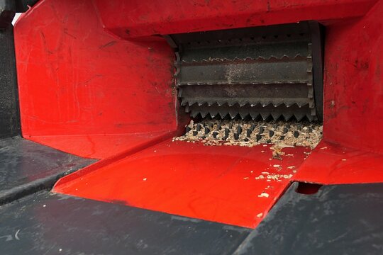 Entrance of perol engine powered larger wood chipper machine, feeding roller visible with some chips of wood. 