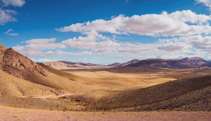 Naklejka premium Vast desert landscape with mountains under a bright blue sky and scattered clouds. Nature and wilderness concept