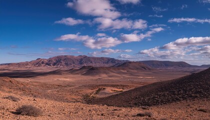Naklejka premium Vast desert landscape with mountains under a bright blue sky and scattered clouds. Nature and wilderness concept