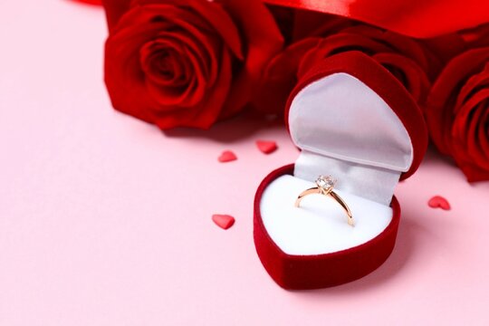 Beautiful shiny gold wedding ring with big diamond gemstone in rich velvet box with red roses on color background