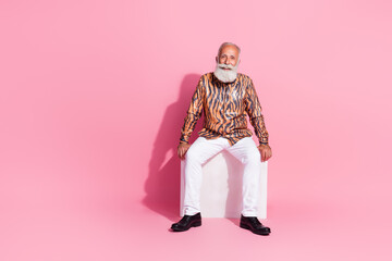 Photo of handsome attractive senior man wear stylish print clothes sit cube empty space isolated on pink color background