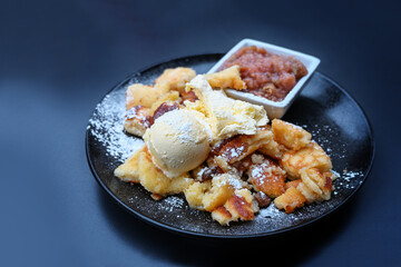 Kaiserschmarrn, fluffy shredded pancake with vanilla ice cream and fruit compote on a dark blue plate, popular dessert in Austria and Bavaria, copy space, selected focus