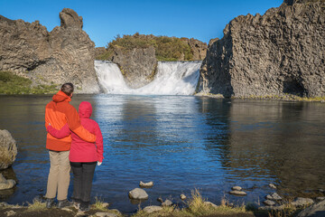 A hiking couple standing at Hjálparfoss Waterfall in Þjórsárdalur. The waterfall is a...