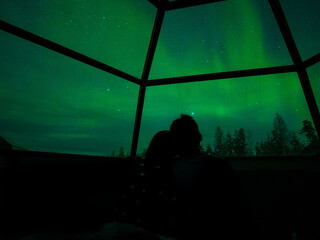 A couple enjoy view of Aurora Borealis and stars in glass igloo in Lapland, Rovaniemi, Finland...