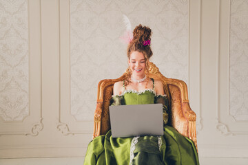 Elegant young woman in a historic costume enjoying modern life on a laptop, merging past and...
