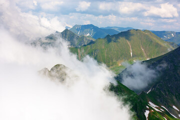 clouds in the mountains. dynamic cloudscape. landscape of transylvania alps on a sunny summer day. scenery with steep rocky slopes with grass and snow. beautiful nature background. picturesque romania