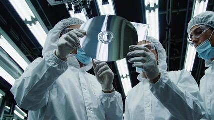 Personnel analyze a semiconductor wafer under bright laboratory lights in a cleanroom environment