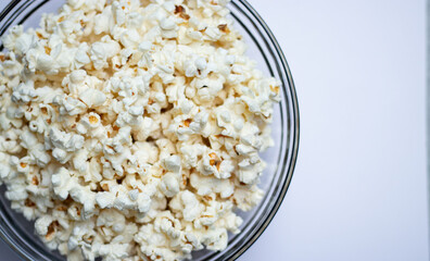 Top view of tasty popcorn in a glass bowl on white table background 