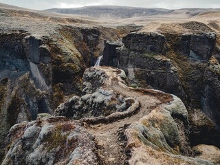 Scenic view of Fjaorargljufur canyon showcasing rugged cliffs and a winding path under a cloudy sky.