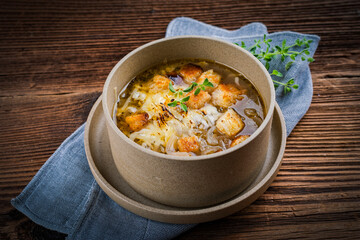 Traditional French onion soup with onion rings, pieces of bread and grated mountain cheese served as a close-up in vegetable broth in a designer plate on a rustic wooden table
