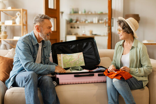 Elderly couple packing suitcase for vacation, senior husband and wife talking while preparing for vacation trip