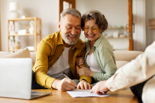 Happy senior couple signing real estate lease contract indoors, elderly man and woman filling paper form, meeting with realtor