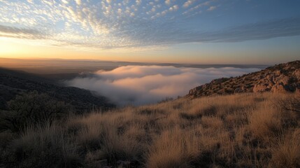 Obraz premium Stunning sunset view over a valley shrouded in fog during a temperature inversion with dramatic cloud formations and golden grass foreground.