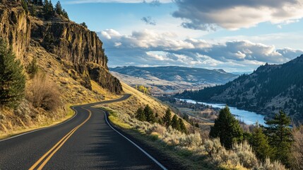 Scenic mountain viewpoint with winding road alongside river and foothills under a dramatic sky in a tranquil landscape setting