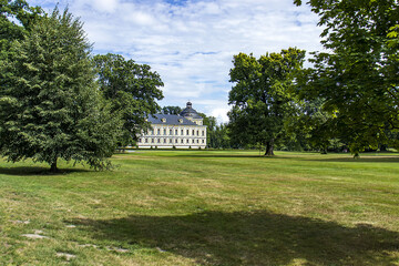 A beautiful and well-kept castle garden. Castle building in the background behind the trees. Historic building. A castle with a castle garden.