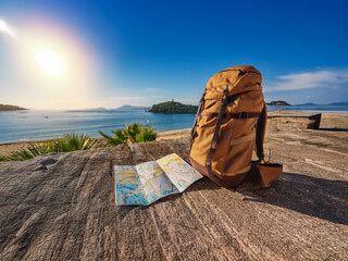 A tan backpack and unfolded map rest on a stone wall overlooking a calm ocean scene under a bright sun.  Ready for adventure!