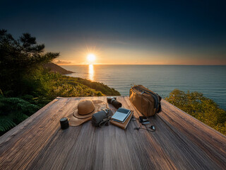 Sunrise over a tranquil ocean, viewed from a wooden deck. Travel essentials hat, camera, journal are neatly arranged, awaiting the day's adventures.