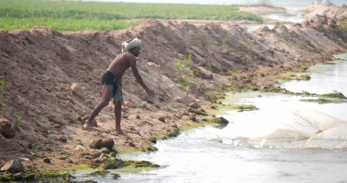 Indian fisherman throwing net into pond to catch fishes a rural countryside.