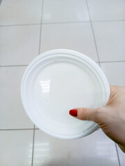 Close-up of white plastic plates in packaging. A hand holds disposable plates for takeout....