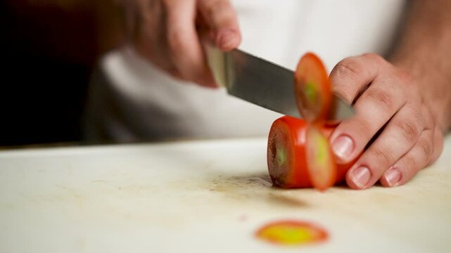 Close-up of a chef slicing a juicy Italian tomato with a sharp knife on a rustic cutting board