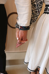 During the wedding ceremony, the bride and groom in embroidered dresses hold hands.