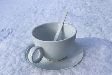 eine weiße Kaffeetasse mit weißen Löffel im Schnee