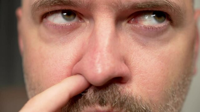 Man picking nose with silly look on face close up. Male digging nose with goofy expression. Guy scratching nose with foolish grin