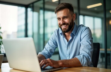 Fototapeta premium Smiling businessman works at modern office using laptop. Businessman in casual attire uses laptop, phone. Happy man looks at computer screen. Bright office interior. Modern workplace. Business person