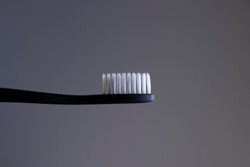 Black toothbrush with White bristles close-up on a gradient gray background
