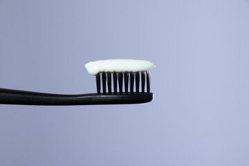 White toothpaste on a Black toothbrush with Black bristles close-up on a gradient gray background