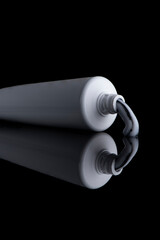 Toothpaste tube shot on a pure black background, on a reflective material. Close-up shot.