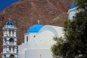 Blue domes and Belfry of the church of Holy Cross in Perissa on a Mesa Vouno mountain background. Greek Orthodox Church in Perissa, Santorini.