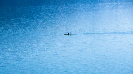 Two men are seen kayaking in a blue lake, enjoying the serenity of the water. The calm environment...