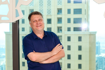 A blond man blue shirt against the backdrop of big city buildings.