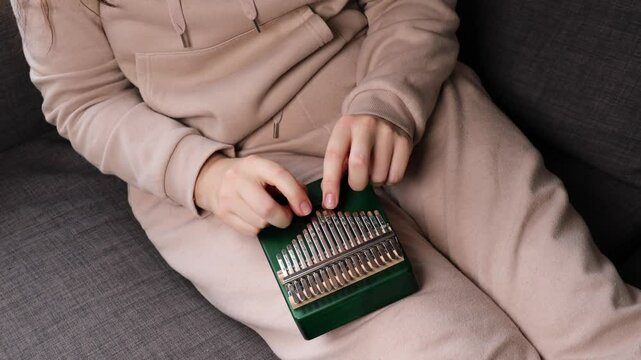 close-up of hands playing a kalimba, plucking the metal tines to produce music on the thumb piano	
