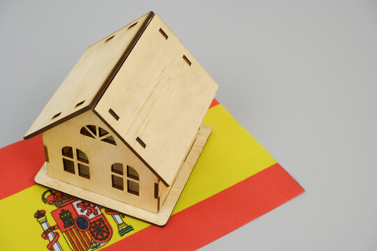 Real estate in Spain. Wooden house model and Spanish flag on gray background.