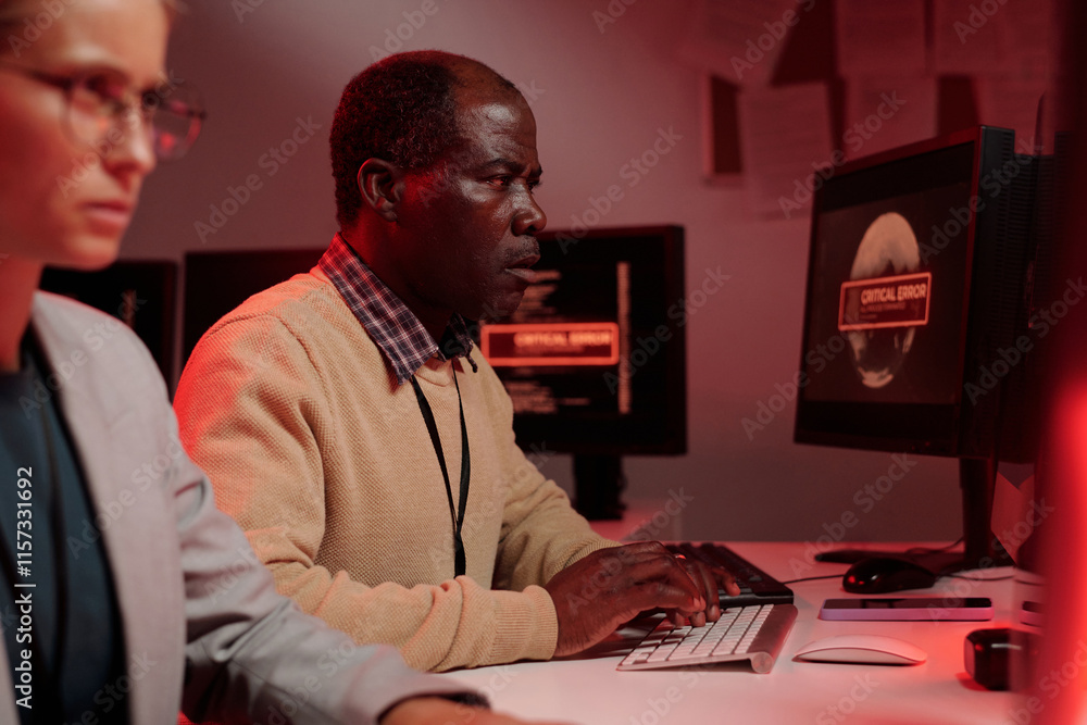 Poster Mature African American male IT manager typing on computer keypad while trying to solve technical problem by workplace