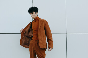 Stylish young man in brown suit posing against a minimalist white background