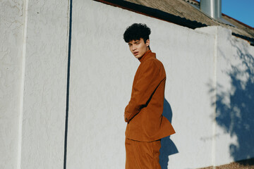 Young man in stylish brown suit against a white textured wall, exhibiting a modern and...