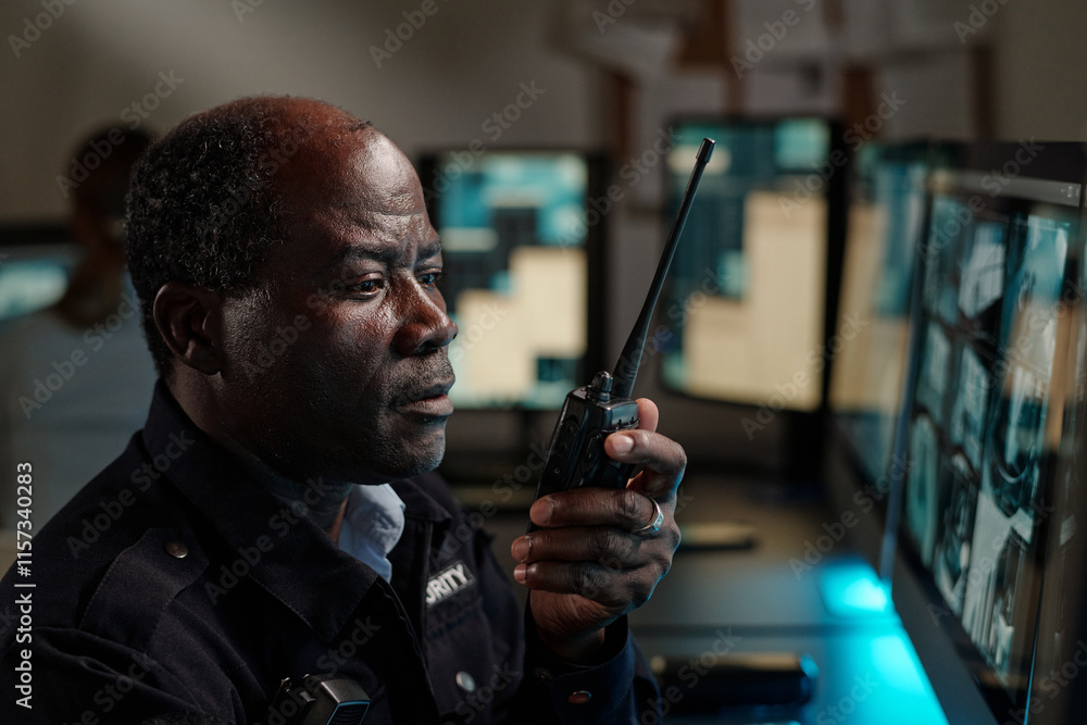 Poster serious mature security guard in uniform looking at computer screen while reporting about situation 