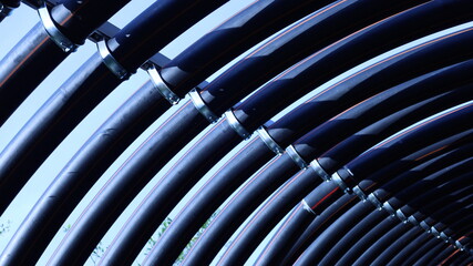 Arranged pipe clamps. Metal clamps hold PE pipes curved to metal pipes in a row in a sunlit bottom view with copy space with selective focus.