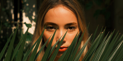 A woman with long brown hair is standing in front of a green bush