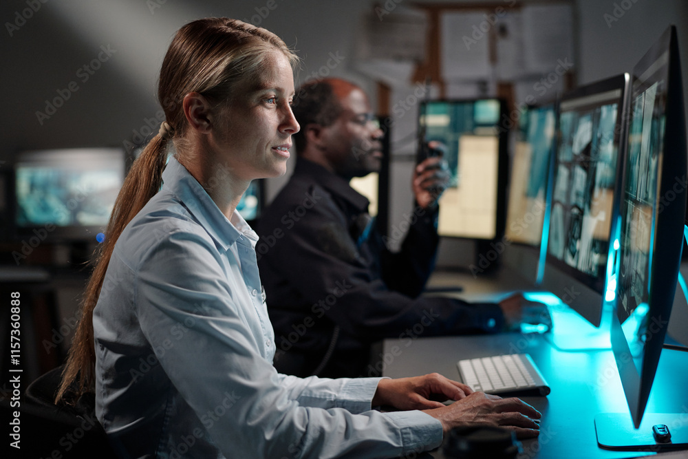 Poster young serious woman in uniform of security officer clicking mouse and looking at desktop computer sc